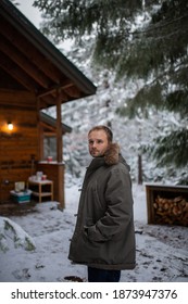 Handsome Man Standing With Cabin And Beautiful Snowy Pines As Background. Portrait Of Serene Man In Calm Snowy Forest. Relaxing Winter Holiday