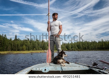 Handsome man is standing on the boat with baddle in his hands and dog near of his legs