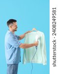 Handsome man steaming clothes with steamer on blue background