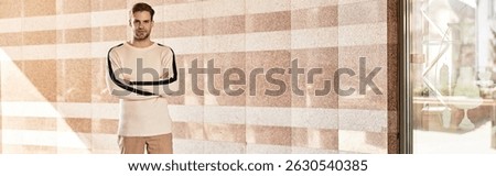 A handsome man strides purposefully alongside a textured wall while sunlight filters around him.