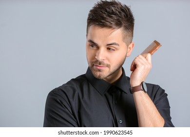 Handsome man with stylish hairdo and comb on grey background - Shutterstock ID 1990623545