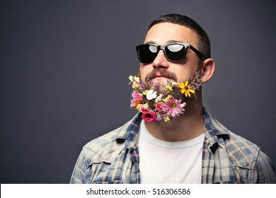 Handsome man in sunglasses with beard of flowers on dark background