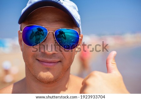 A handsome man in sunglasses gives a close-up thumbs-up. The reflection in the sunglasses.