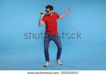 Handsome man with sunglasses and microphone singing on light blue background