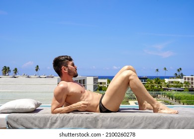 The handsome man in sunglasses with naked torso lies near the pool