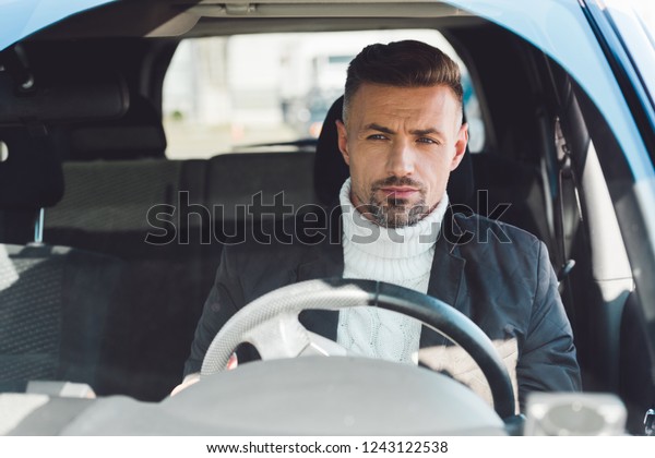 Handsome man in\
sweater and jacket sitting in car\
