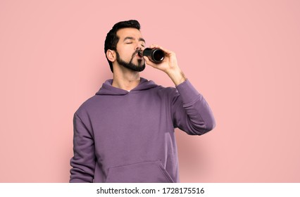 Handsome Man With Sweatshirt Drinking Beer Over Isolated Pink Background