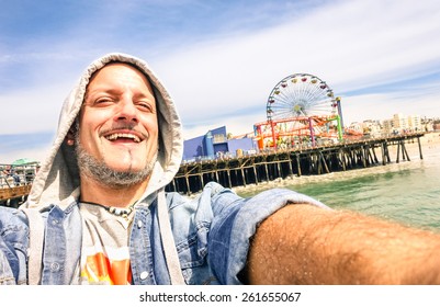 Handsome man taking a selfie at Santa Monica Pier with ferris wheel - Sunny day in California coast - Adventure travel lifestyle around United States of America - Composition with tilted horizon