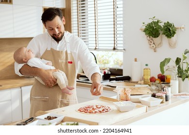 Handsome man talking with lovely baby holding in arms. Adorable father in aprons cooking preparing homemade pizza dressing dough applying tomato sauce. - Powered by Shutterstock