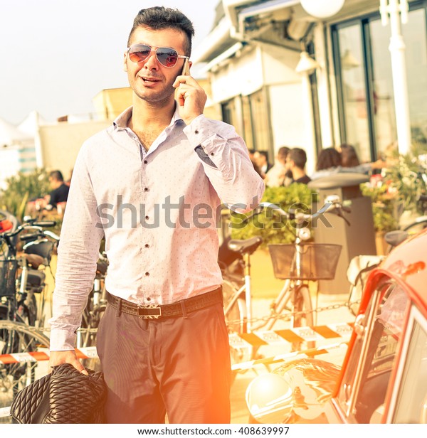 Handsome\
man talking on mobile phone - Fashion male model walking on street\
next to sport car - Concept of self confidence and successful life\
style - Sun halo and soft vintage filter\
look