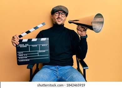 Handsome Man With Tattoos Holding Video Film Clapboard And Louder Clueless And Confused Expression. Doubt Concept. 