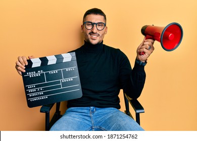 Handsome Man With Tattoos Holding Video Film Clapboard And Megaphone Clueless And Confused Expression. Doubt Concept. 