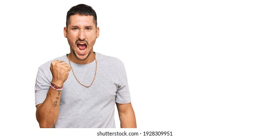 Handsome man with tattoos wearing 90s style angry and mad raising fist frustrated and furious while shouting with anger. rage and aggressive concept.  - Shutterstock ID 1928309951