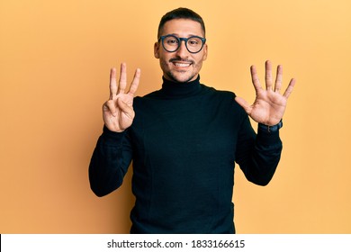 Handsome man with tattoos wearing turtleneck sweater and glasses showing and pointing up with fingers number eight while smiling confident and happy. 