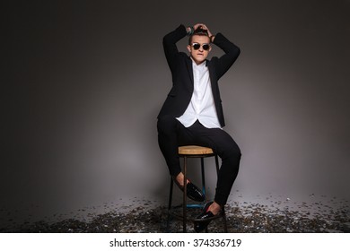 Handsome man in trendy cloth sitting on the chair over black background