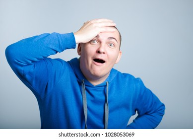 Handsome Man Unpleasantly Surprised Clutching His Head, Wearing A Blue Hoodie, Isolated Photo On The Background