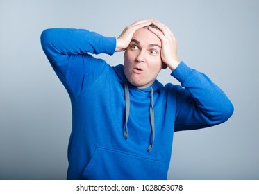 Handsome Man Unpleasantly Surprised Clutching His Head, Wearing A Blue Hoodie, Isolated Photo On The Background