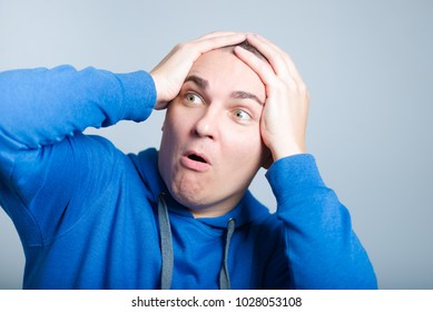 Handsome Man Unpleasantly Surprised Clutching His Head, Wearing A Blue Hoodie, Isolated Photo On The Background