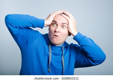 Handsome Man Unpleasantly Surprised Clutching His Head, Wearing A Blue Hoodie, Isolated Photo On The Background