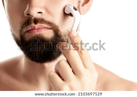 Handsome man using meso roller for better beard growth on white background