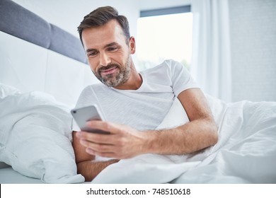 Handsome man using phone in bed after waking up in the morning