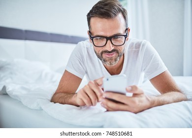 Handsome Man Using Phone Lying On Bed In The Morning