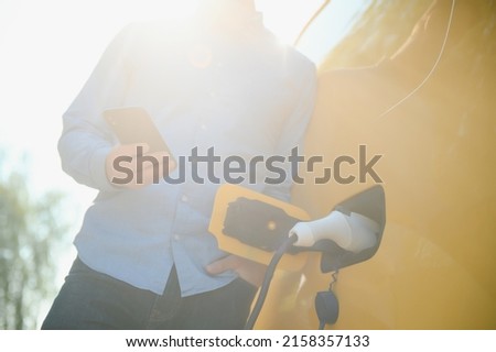 Handsome man using phone while car being charged.