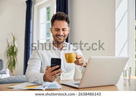 Handsome man using smartphone and drinking coffee while working from home