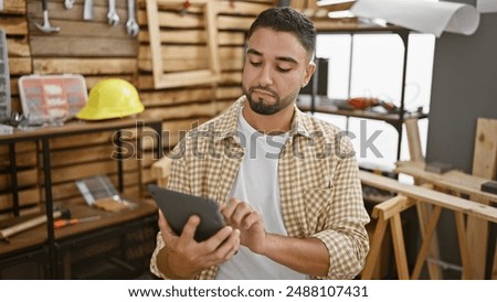 Handsome man using tablet in a carpentry workshop, surrounded by tools and wood.