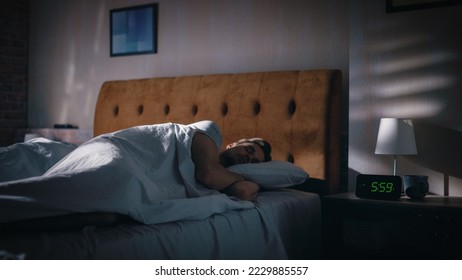 Handsome Man Wakes Up and Turns off Alarm Clock. Proceeds to Have a Productive Day of Work. Stylish Apartment. Focus on the Clock Showing Five Hours and Fifty Nine Minutes in the Morning - Powered by Shutterstock