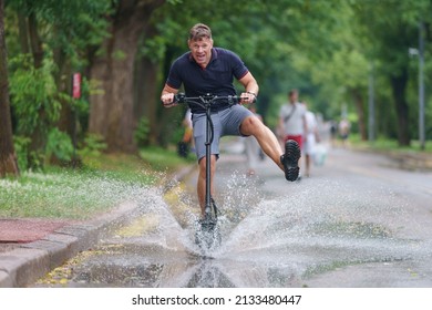Handsome man walking in the Moscow public park in summer day aftre the rain. Water splashes from the puddle around him. He riding motor scooter. Leisure time concept. Frontal view