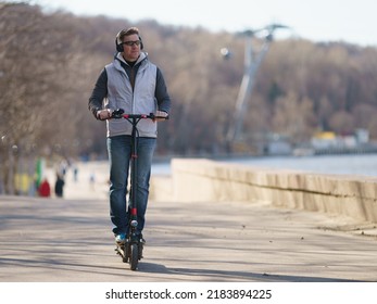 Handsome Man Walking In Moscow Public Park In Sunny Spring Day. He Is Well-dressed, Put On Sunglasses. His Clothes Is In Gray Colors. He Riding Motor Scooter And Admiring View. Healthy Lifestyle