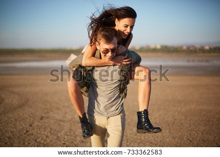 Handsome man walking with pretty girl on a back on a natural background. Romantic trip concept. Copy space.