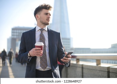 Handsome man walking in the street, checking his phone and drinking coffee - Powered by Shutterstock