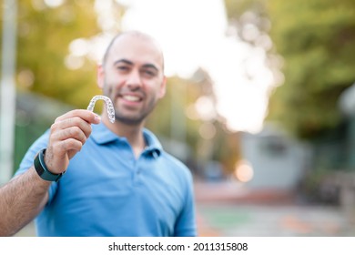 Handsome man with warm smiling is holding an invisaligner. Includes copy and text space.
