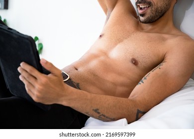 Handsome man watches an adult video on a tablet while sitting on the bed. Concept of porn, men's needs and loneliness.