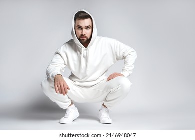 Handsome man wearing blank white hoodie and pants sitting on light gray background - Shutterstock ID 2146948047