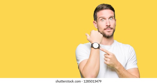 Handsome man wearing casual white t-shirt In hurry pointing to watch time, impatience, upset and angry for deadline delay