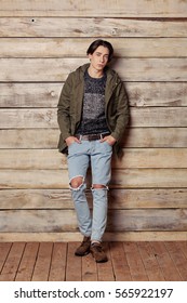 Handsome man wearing green jaket and torn jeans in wooden rural house interior