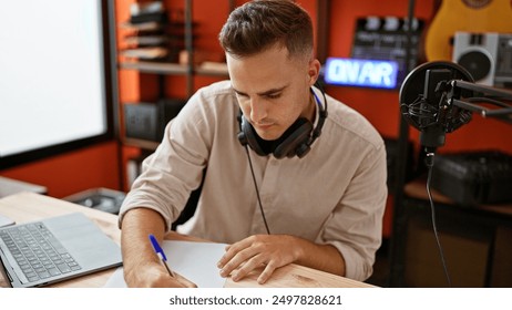 Handsome man wearing headphones concentrating on writing music in a modern studio setup. - Powered by Shutterstock