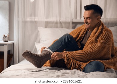 Handsome man wearing warm socks in bedroom at night