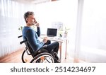 Handsome man in wheelchair working from home office, making phone call. Telecommuting and home office.