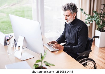 Handsome man in wheelchair working from home office, using computer in office. Telecommuting and home office.