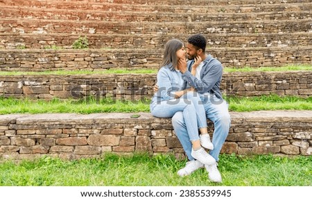 A handsome man whispering to a beautiful smiling woman how much he loves her as they are sitting in the park