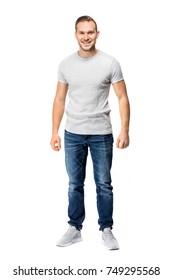 Handsome Man In A White T-shirt, Looking Cheerful, Smiling Straight Into The Camera. Full Body Studio Shot.