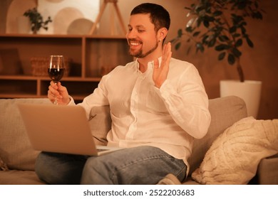 Handsome man with wine and laptop having online date on sofa at home in evening - Powered by Shutterstock