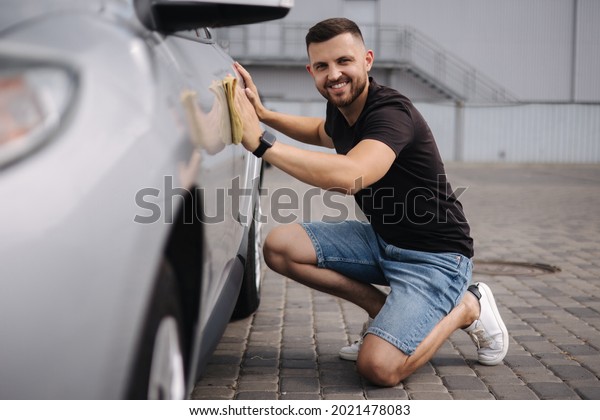 Handsome man wipes a car with a rag in a\
showroom at a self-service car wash. Gray\
car