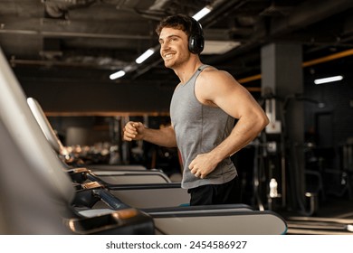 Handsome man in wireless headphones jogging on treadmill at gym and listening music while running, enjoying workout, copy space - Powered by Shutterstock