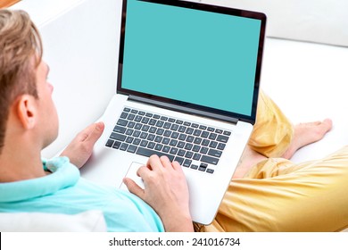 Handsome man working with laptop laying on the couch at home. Empty display for your screenshot