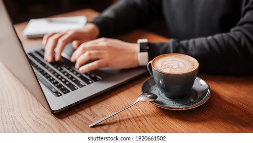 Handsome man working on laptop in the workplace. Businessman prints information at desk with coffee - Powered by Shutterstock